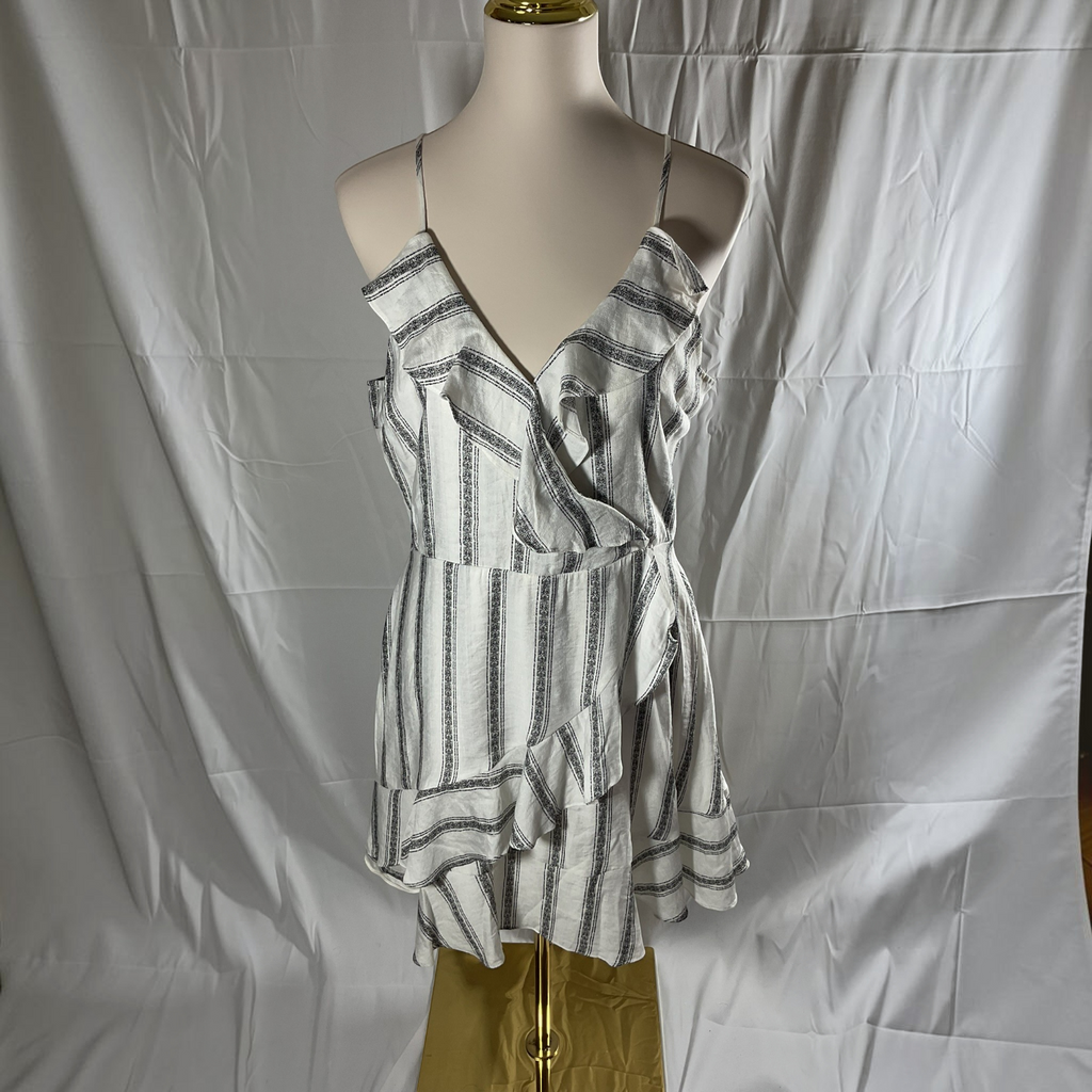 A sleeveless ruffled wrap-style top with thin spaghetti straps and vertical gray stripes on a white base, displayed on a mannequin torso against a wrinkled white fabric backdrop.
