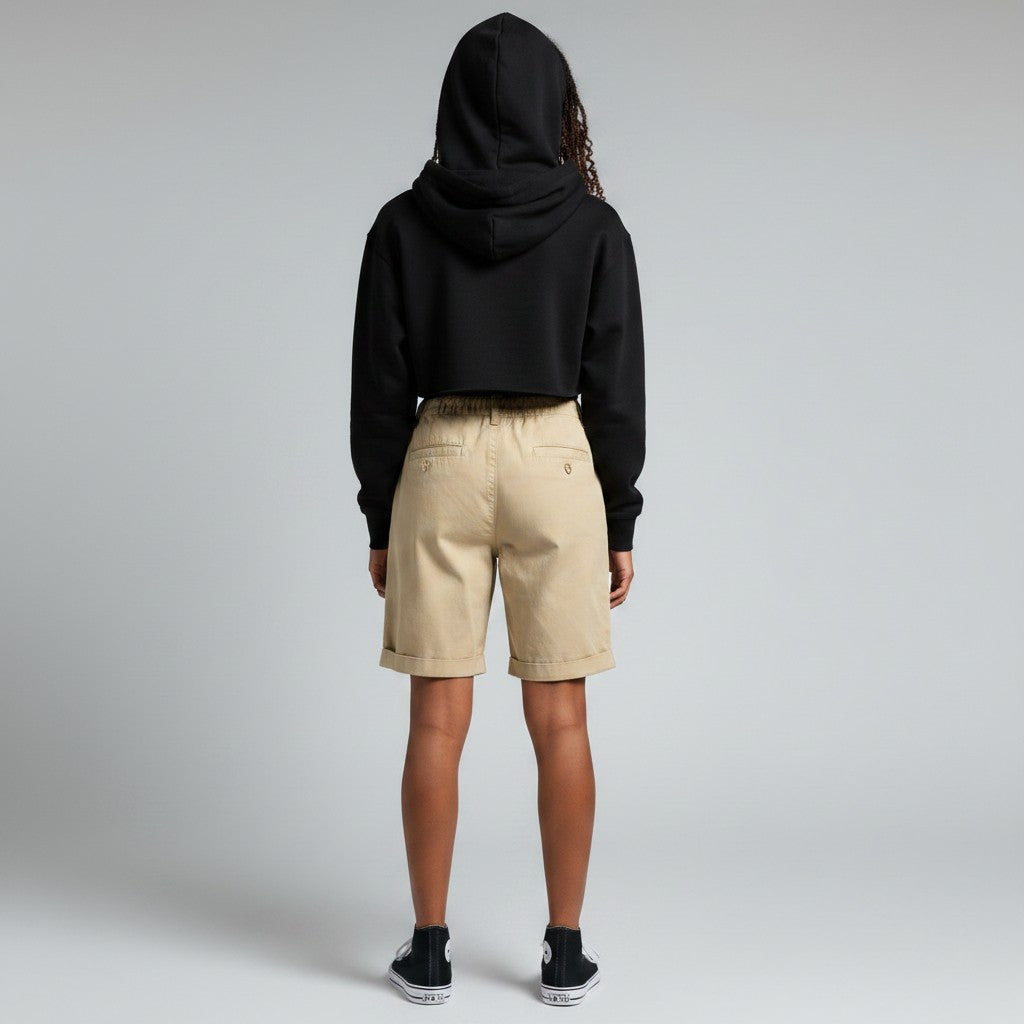 A model shown from the back wearing a black cropped hoodie, beige shorts, and black sneakers against a light gray studio background.