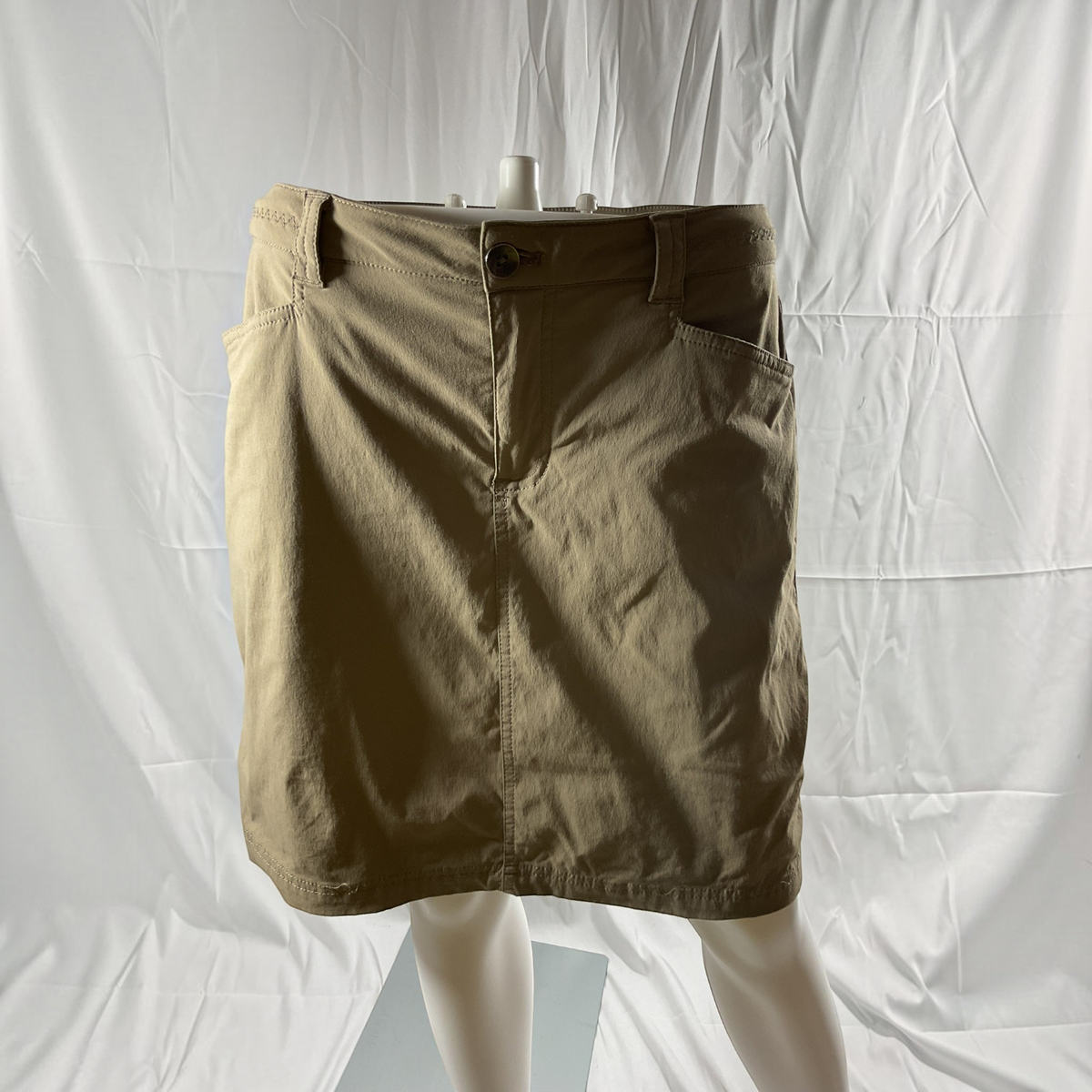 A beige mini skirt with a button closure, belt loops, and front pockets, laid flat on a light gray background.