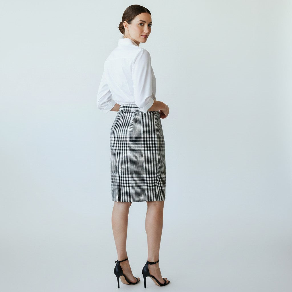 A woman wearing a white shirt with a black ad white skirt and black heels on a light gray background