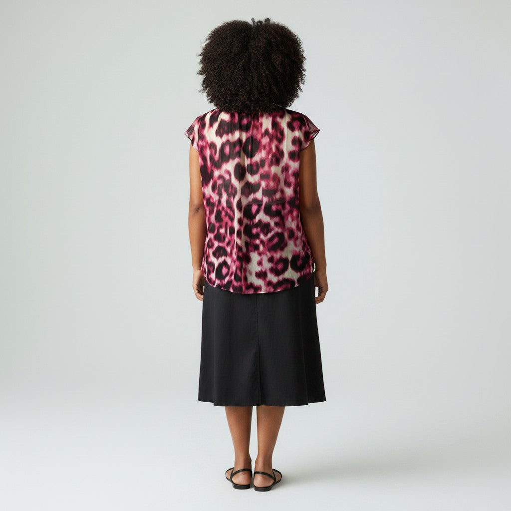 A woman viewed from the back wearing a sleeveless leopard-print top with a pink, black, and beige pattern, paired with a black midi skirt and black sandals, against a light gray studio background.