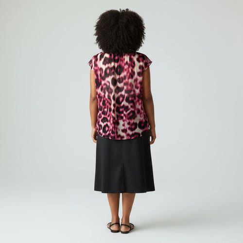 A woman viewed from the back wearing a sleeveless leopard-print top with a pink, black, and beige pattern, paired with a black midi skirt and black sandals, against a light gray studio background.