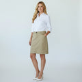 A woman modeling a white button-down shirt and a knee-length beige skirt with front patch pockets, paired with white heels, against a light gray studio background.