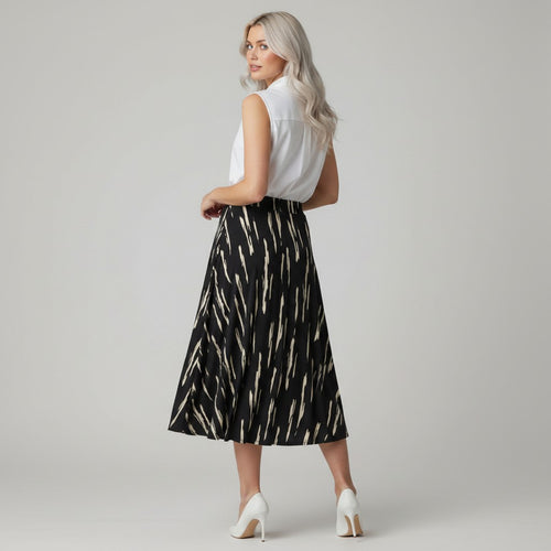A woman modeling a sleeveless white top and a black midi skirt with a beige abstract brushstroke pattern, paired with white high heels, against a light gray studio background.