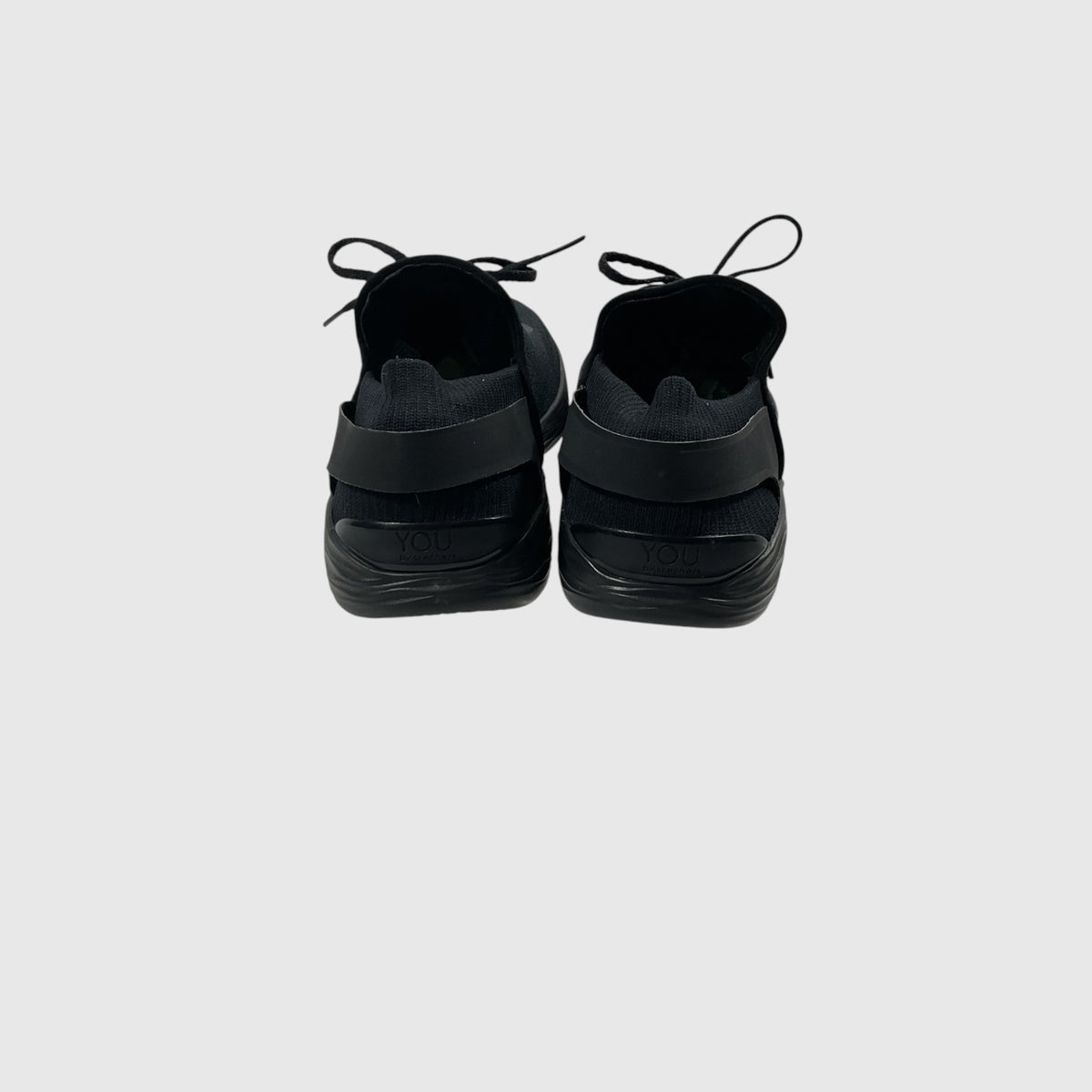 A pair of black slip-on sneakers shown from the back against a light gray background.