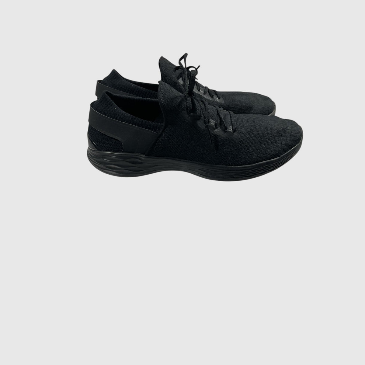 A pair of black slip-on athletic sneakers with textured uppers and black laces, shown from a side profile against a light gray background.
