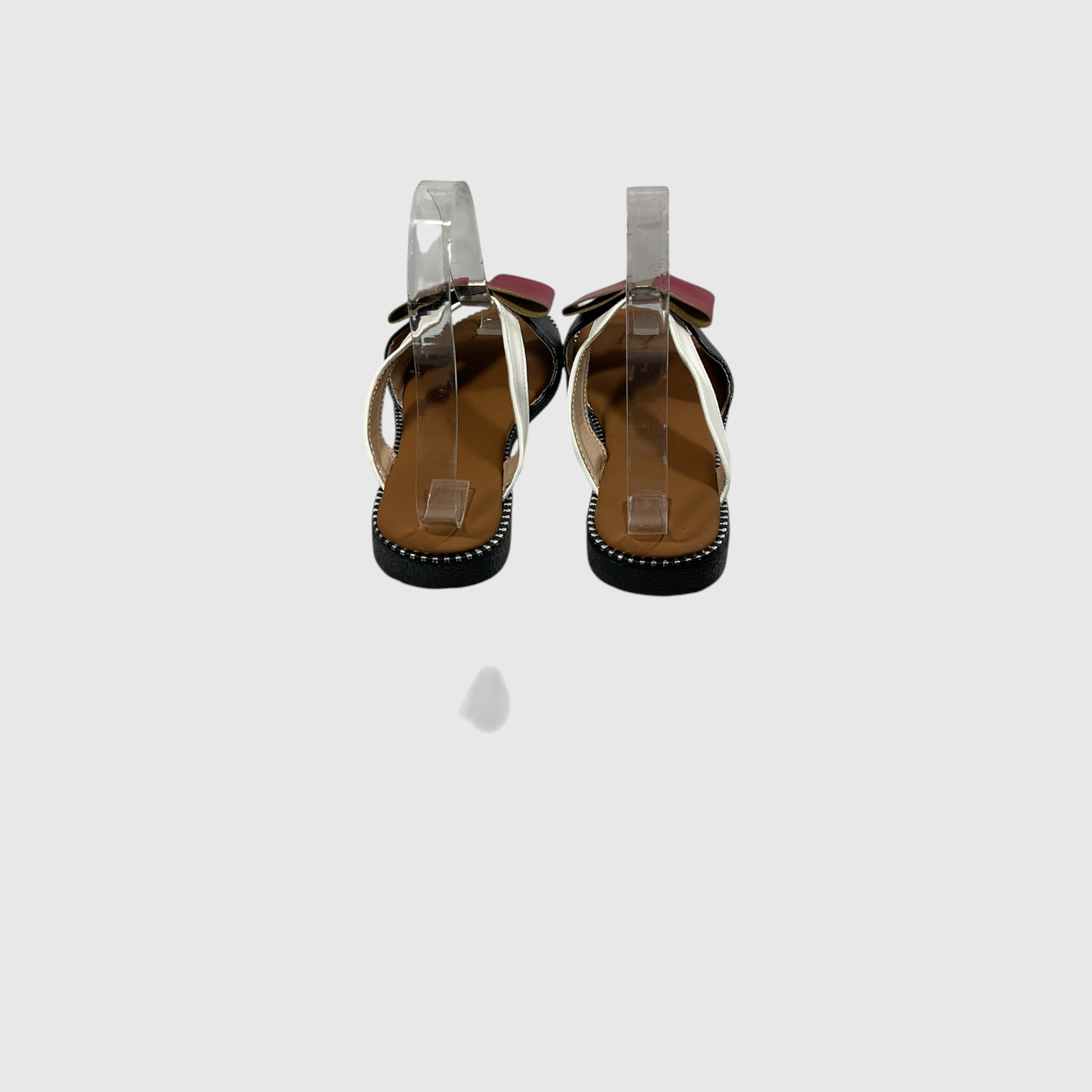 A pair of women's flat sandals shown from the back, featuring clear plastic straps, a tan insole, black outsole, and a small pink bow detail at the top.