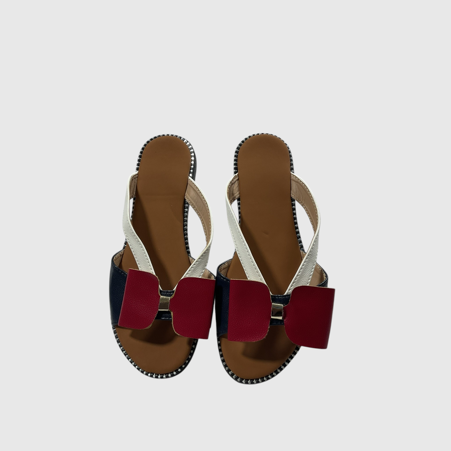 A pair of women's slide sandals with white straps, a navy blue heel tab, and a large red bow detail across the front, shown from a top-down view on a light gray background.