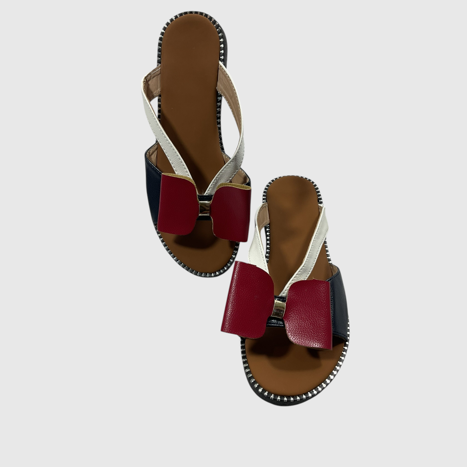 A pair of women's flat sandals with a color-blocked design featuring burgundy, navy blue, and off-white straps, set against a light gray background.