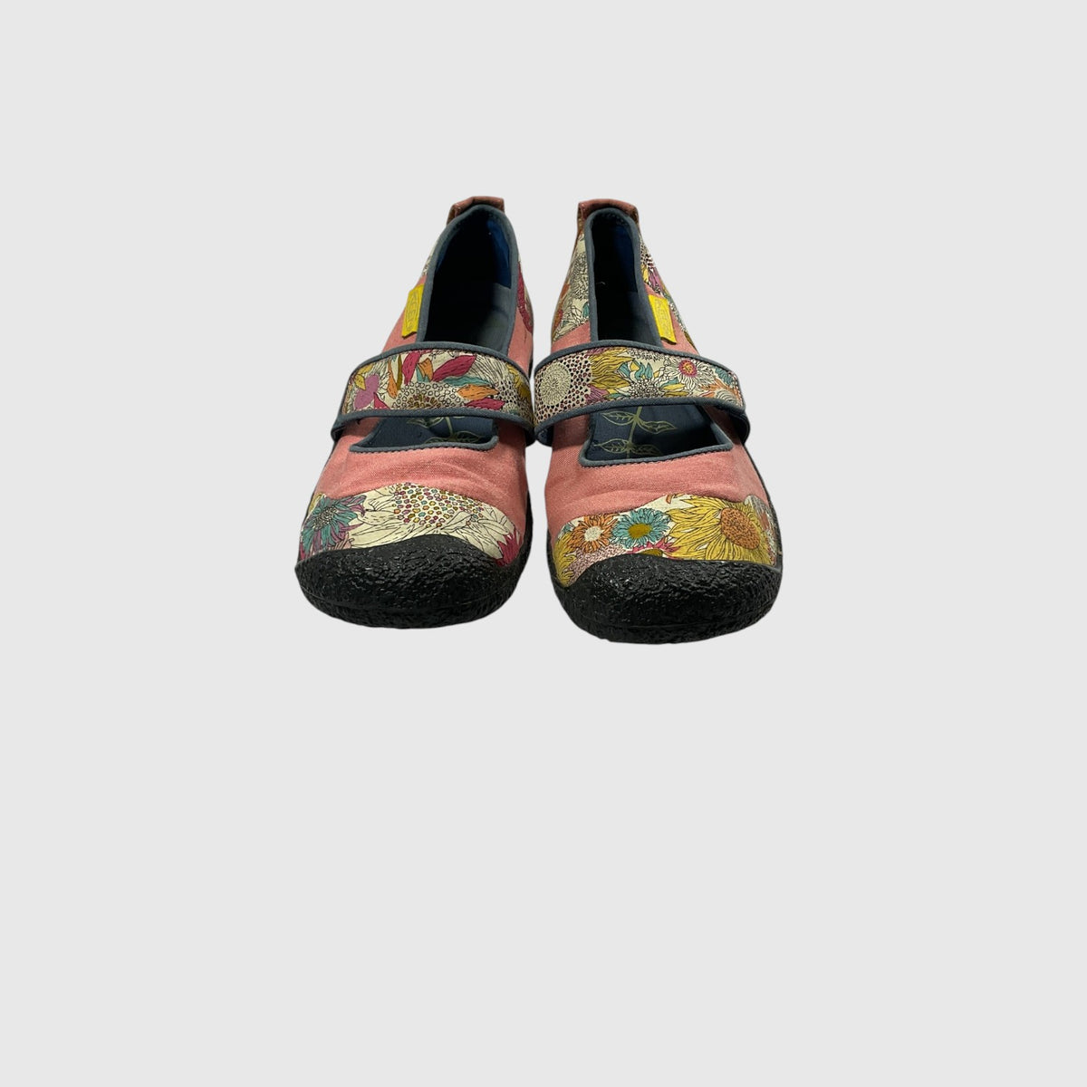 A pair of women's Mary Jane style shoes featuring a dusty pink fabric upper, a wide hook-and-loop strap with a multicolor floral and geometric print, and black rubber soles, shown against a plain light gray background.