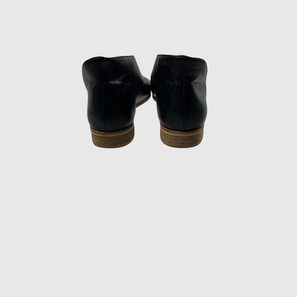 A pair of black leather ankle boots shown from the back, featuring low brown stacked heels, against a solid light gray background.