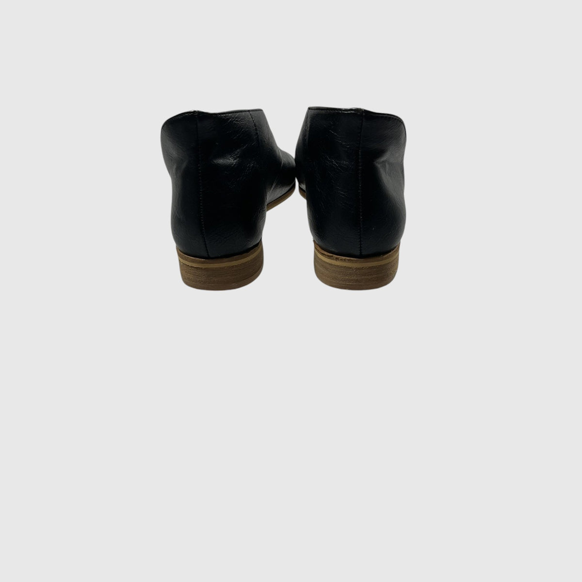 A pair of black leather ankle boots shown from the back, featuring low brown stacked heels, against a solid light gray background.