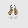A pair of metallic gold T-strap sandals with adjustable ankle straps, displayed on a light gray reflective surface.