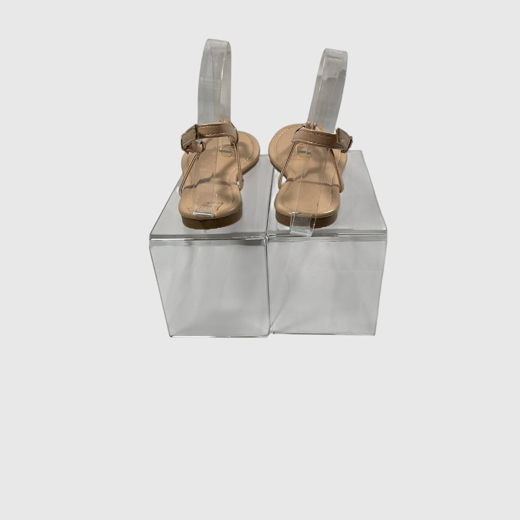 A pair of metallic gold T-strap sandals with adjustable ankle straps, displayed on a light gray reflective surface.