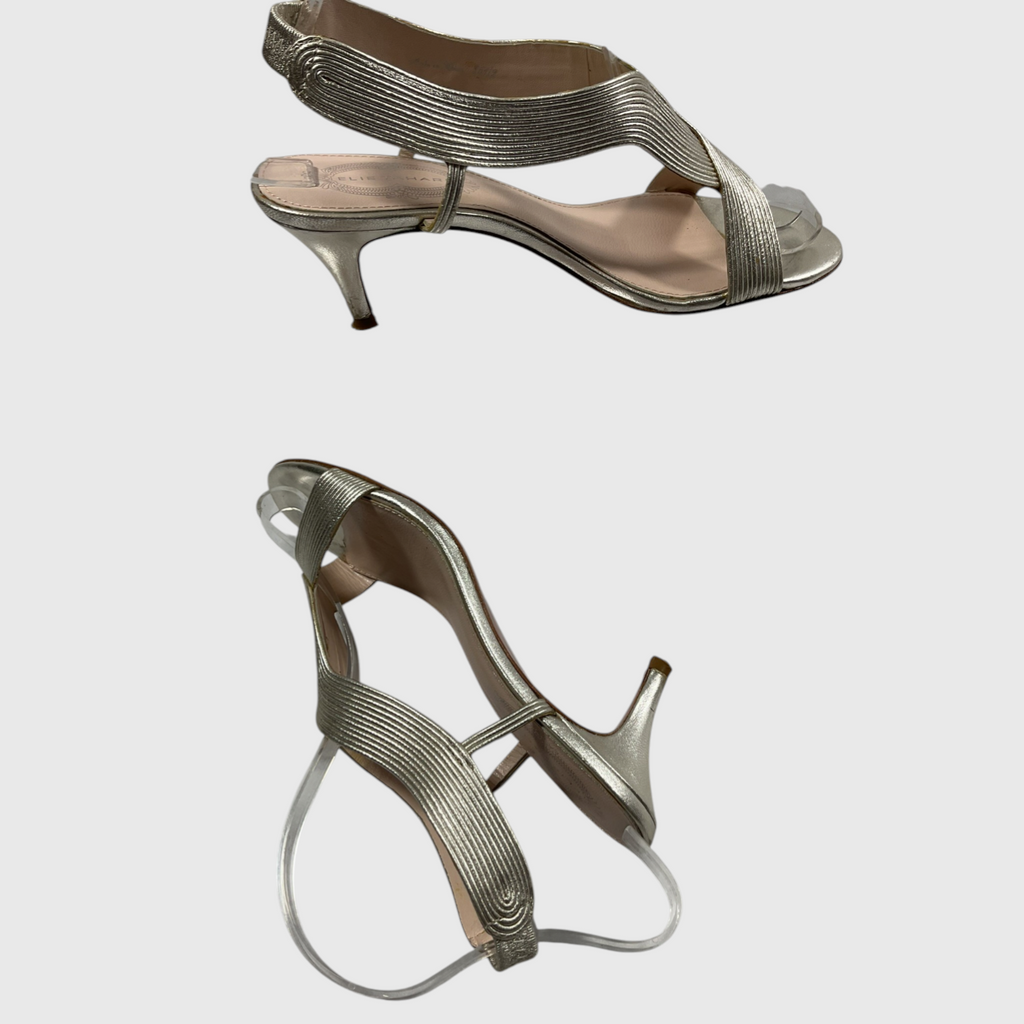 A pair of metallic silver strappy high-heeled sandals shown from two angles against a light gray background.