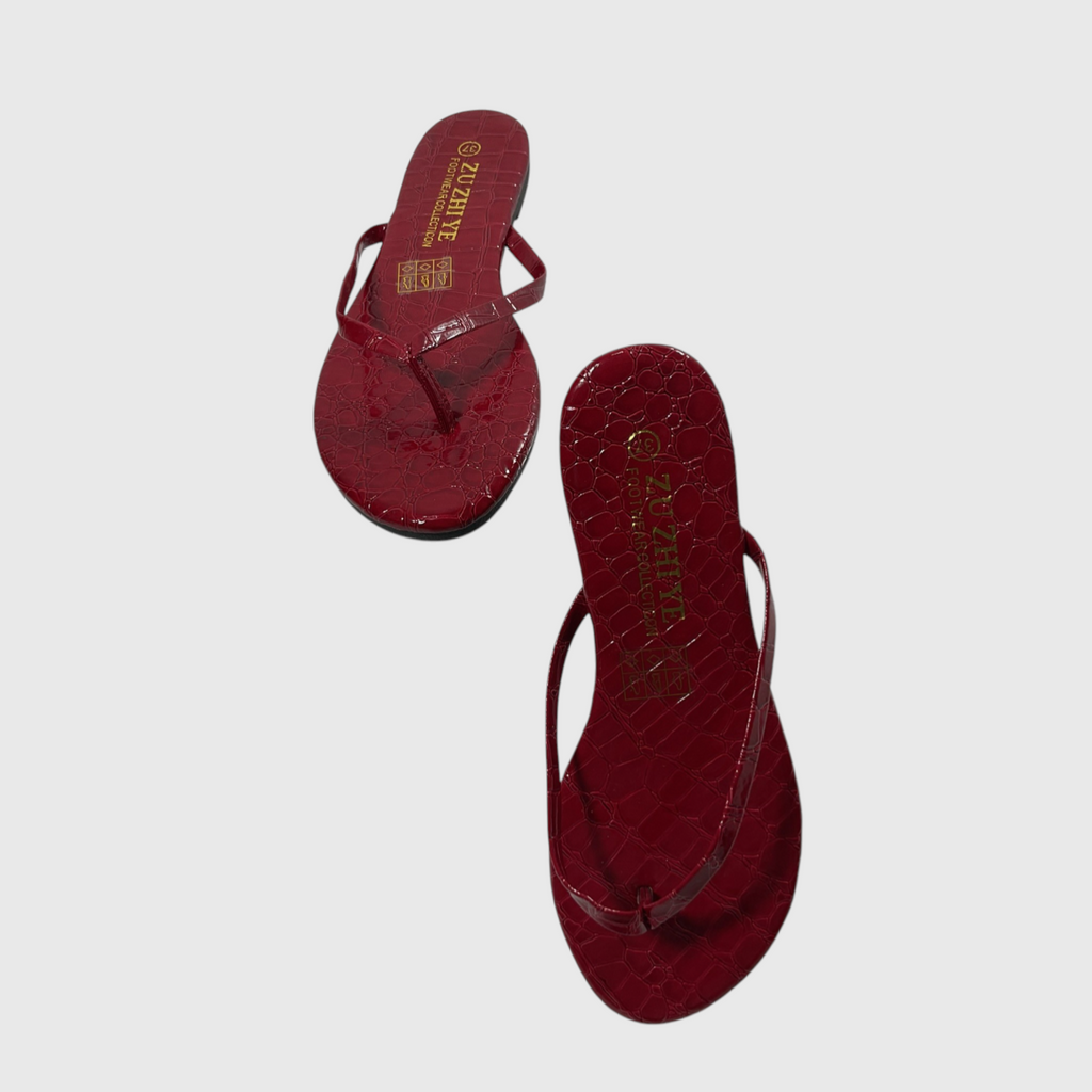 A pair of red crocodile-embossed thong sandals with gold brand lettering, displayed on a light gray background.
