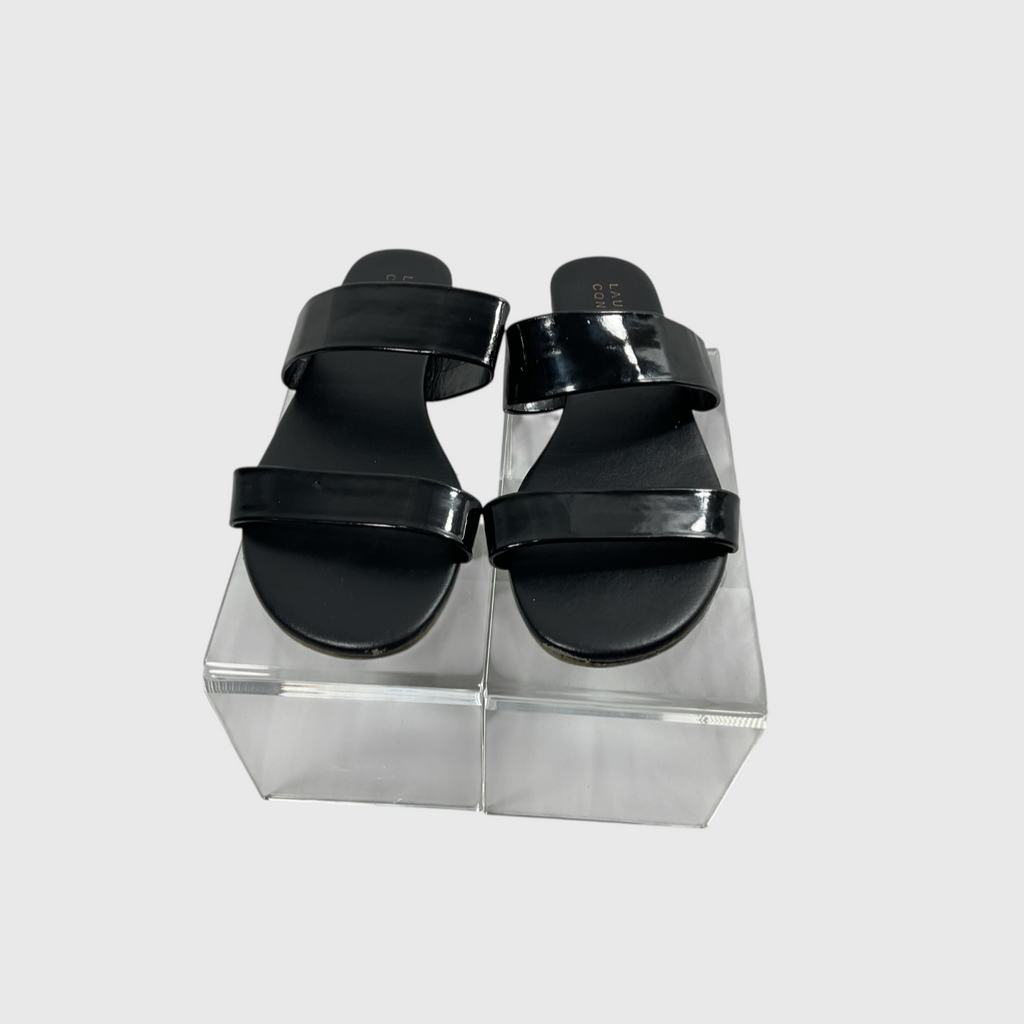 A small black circular mechanical component with a metal mounting tab and a short black side tab, photographed on a white background with a white paper sheet underneath.