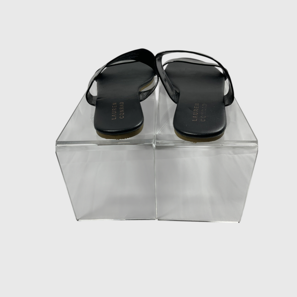 A pair of black flat thong sandals displayed on a clear acrylic block against a light gray background. The brand name 'LEATHER CRAFT' is printed on the insoles.
