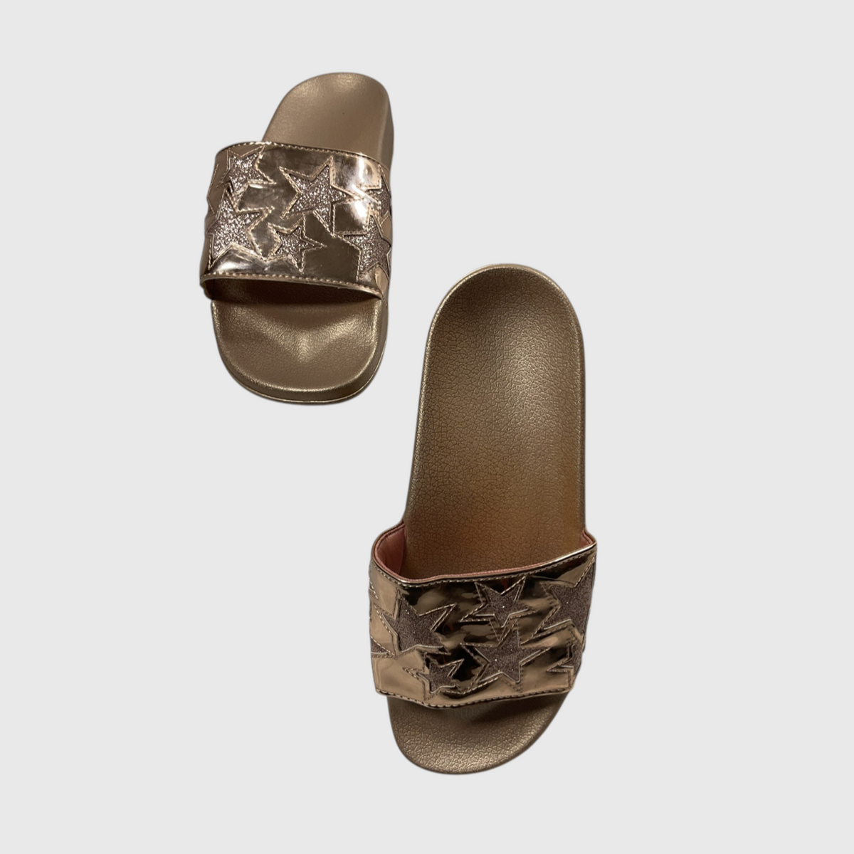 A pair of metallic rose gold slide sandals with star-shaped metallic embellishments on the straps, shown against a light gray background.
