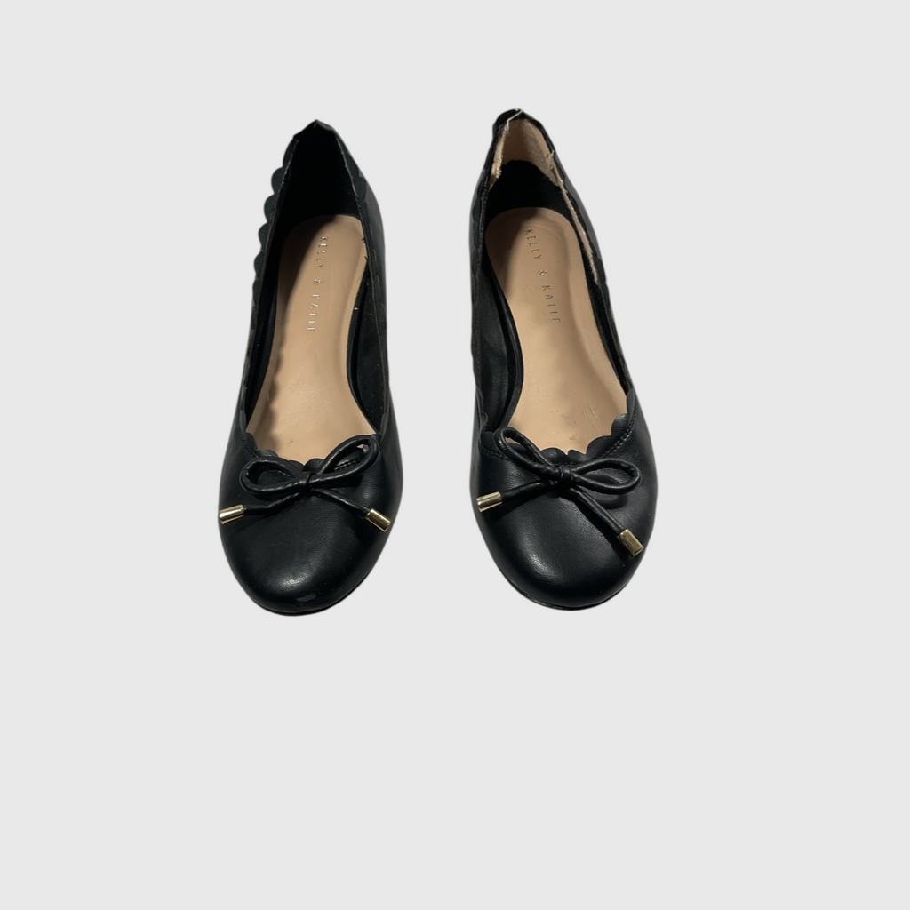 A pair of black leather ballet flats with scalloped edges, bow details, and small gold-tone metal accents on the toes, shown against a light gray background.