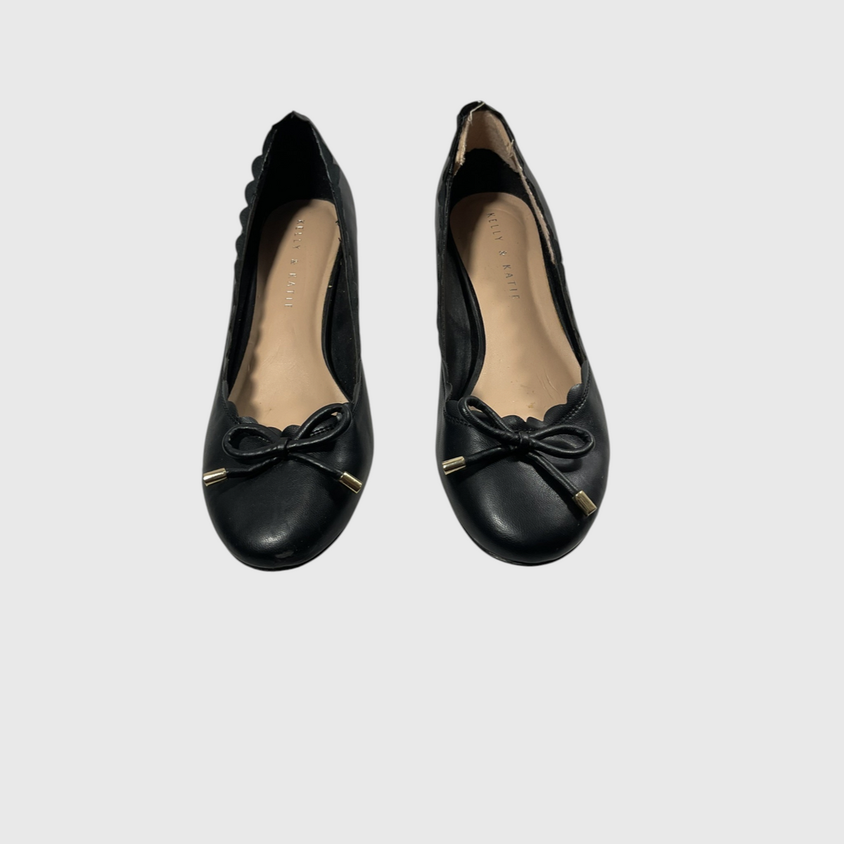 A pair of black leather ballet flats with scalloped edges, bow details, and small gold-tone metal accents on the toes, shown against a light gray background.