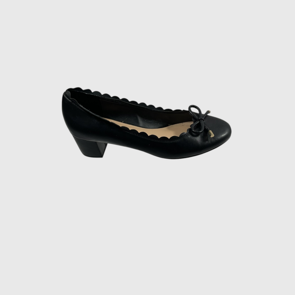 A single black leather pump shoe with a scalloped inner edge and a small bow detail on the toe, shown against a light gray background.