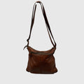 A brown leather shoulder bag with a long adjustable strap, a front zippered pocket, and a slouchy slouchy silhouette, shown against a plain light gray background.