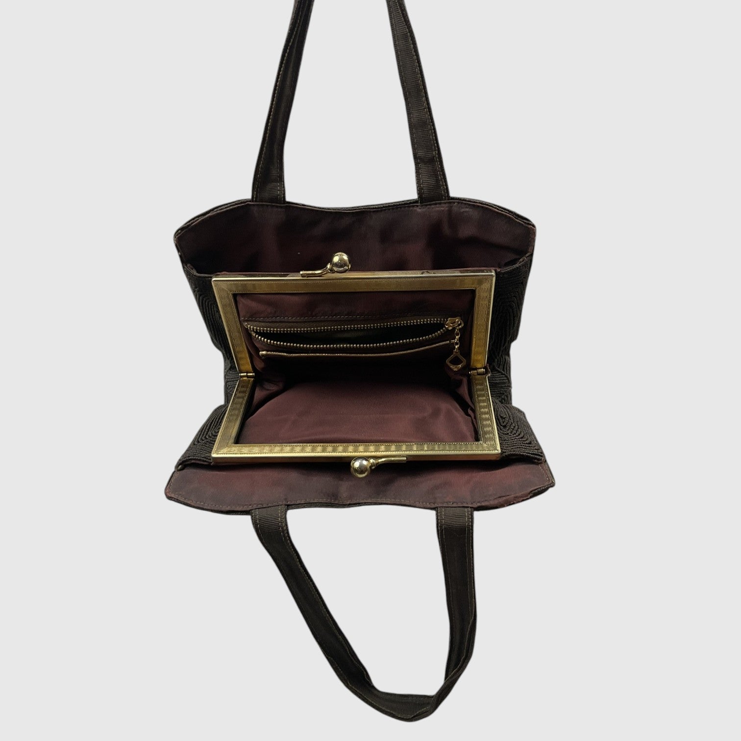 A dark plum purple handbag with black straps and a gold-tone metal frame, shown open to display its interior zippered pocket and lining against a light gray background.
