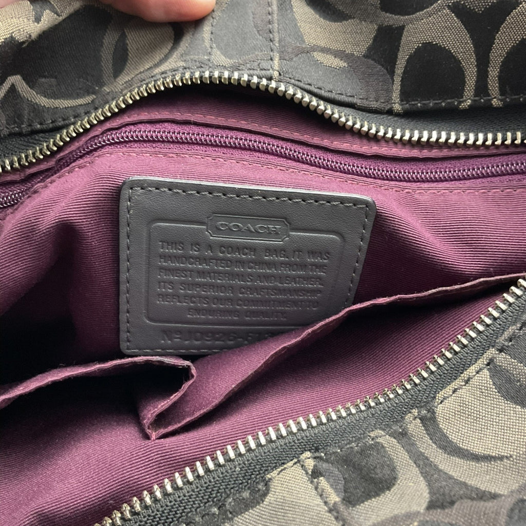 Close-up of a Coach bag interior showing a mauve purple nylon lining with a gray leather brand patch and a gray and beige monogram patterned fabric exterior.