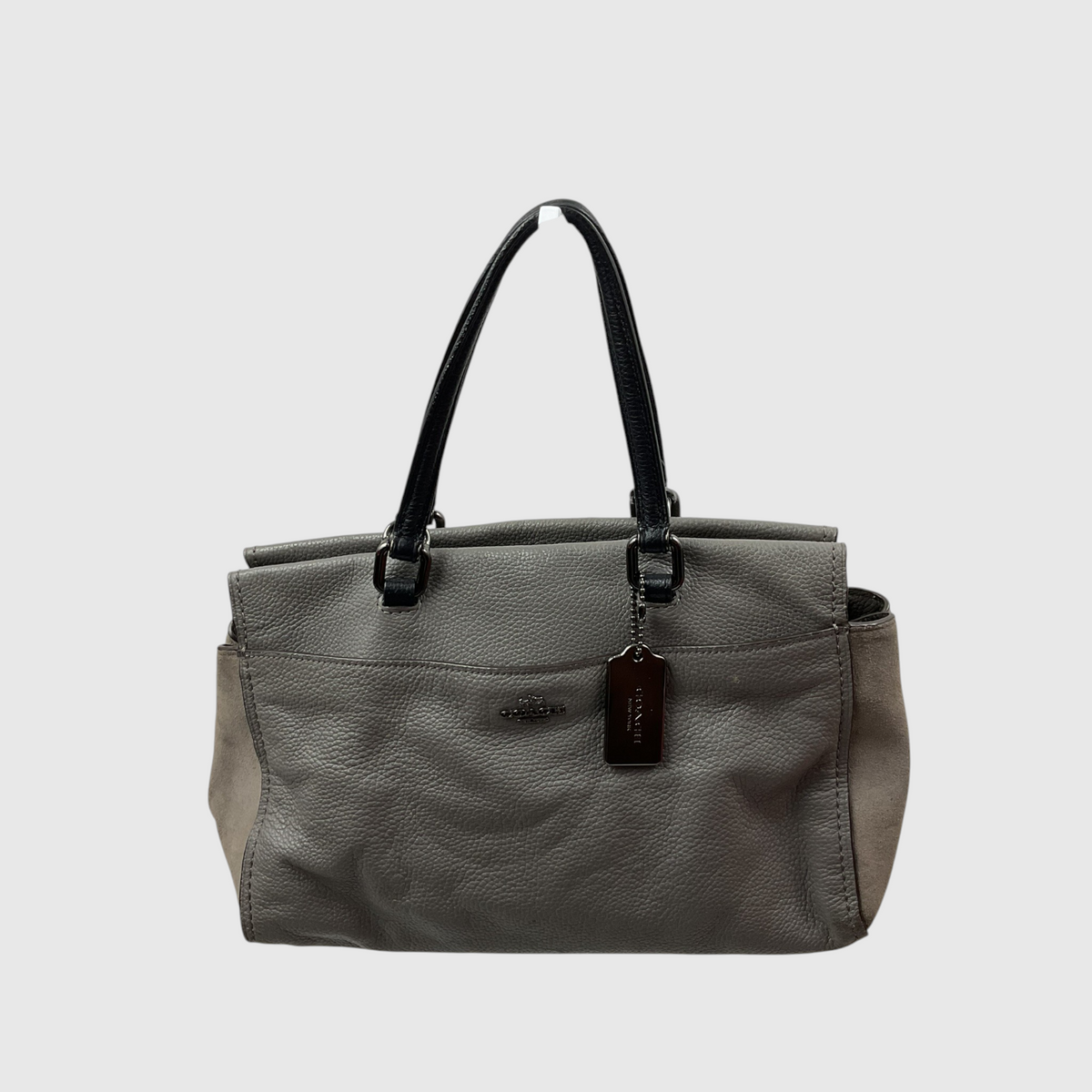  gray canvas tote bag with dark brown leather trim and shoulder strap, worn crossbody against a light gray studio background.