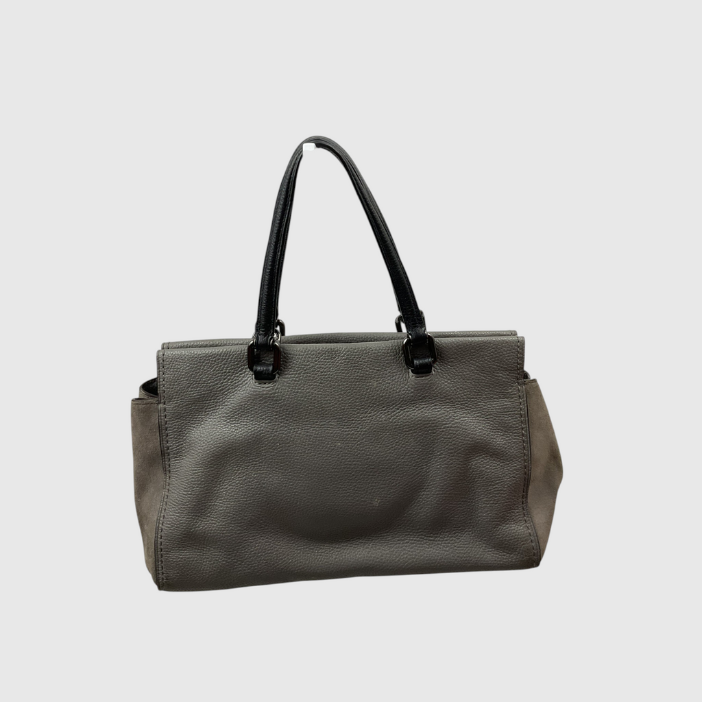  gray canvas tote bag with dark brown leather trim and shoulder strap, worn crossbody against a light gray studio background.