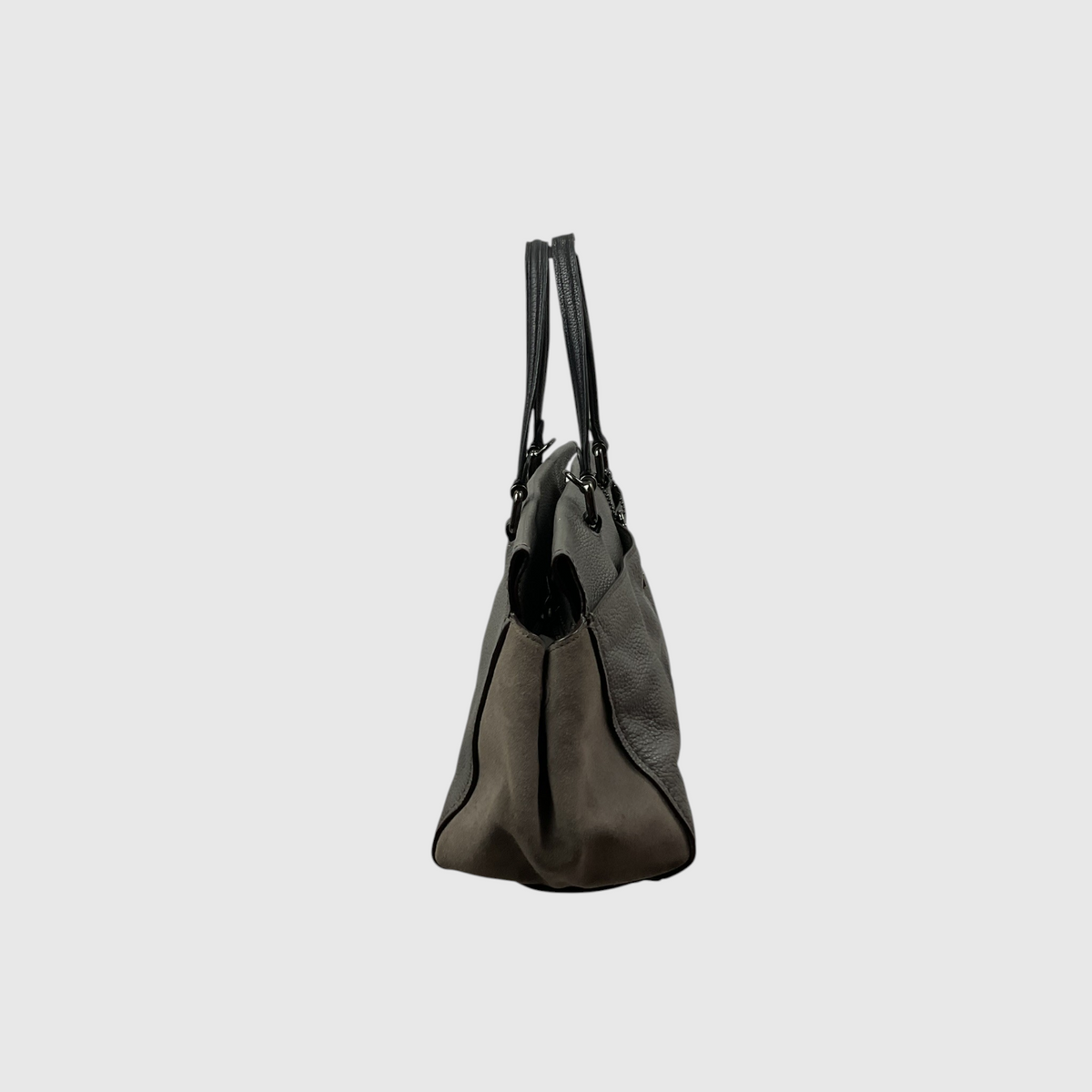  gray canvas tote bag with dark brown leather trim and shoulder strap, worn crossbody against a light gray studio background.