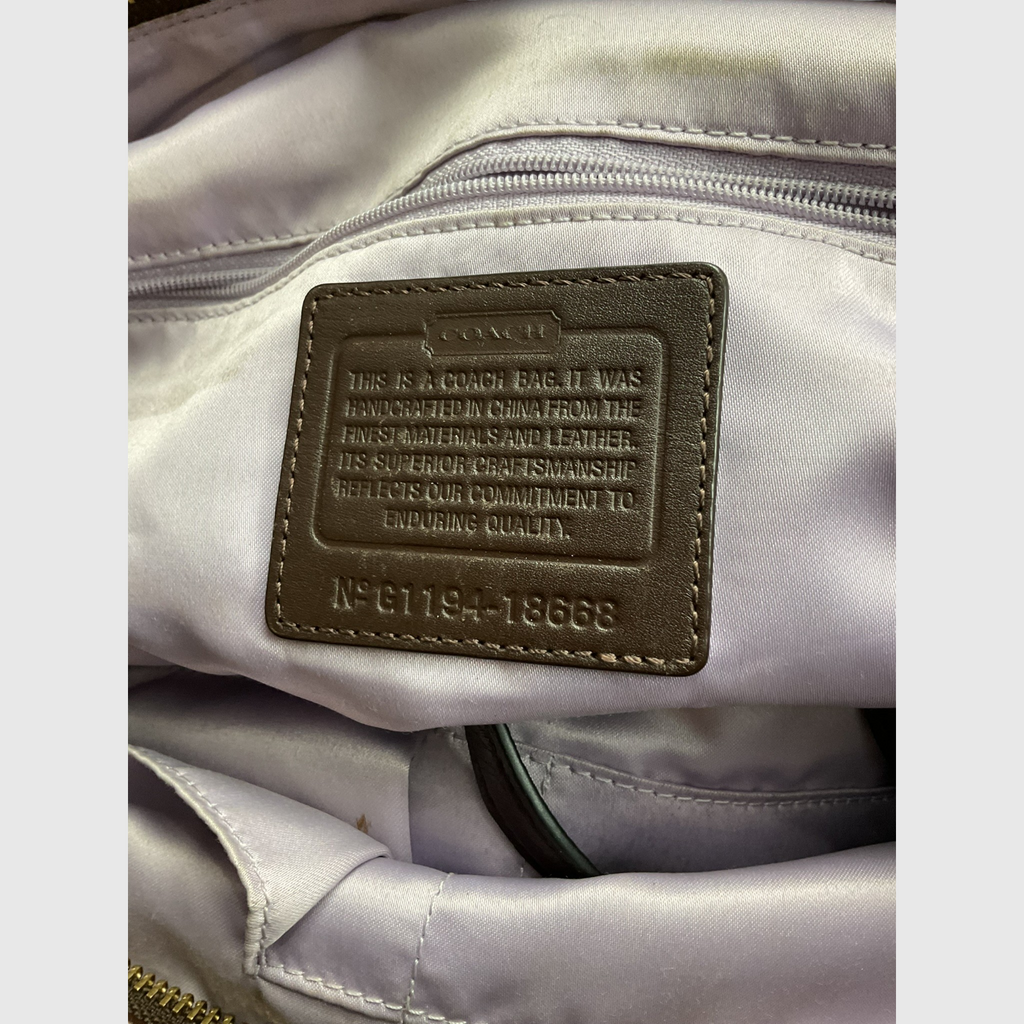 The interior of a gray canvas tote bag with dark brown leather trim and shoulder strap, worn crossbody against a light gray studio background.