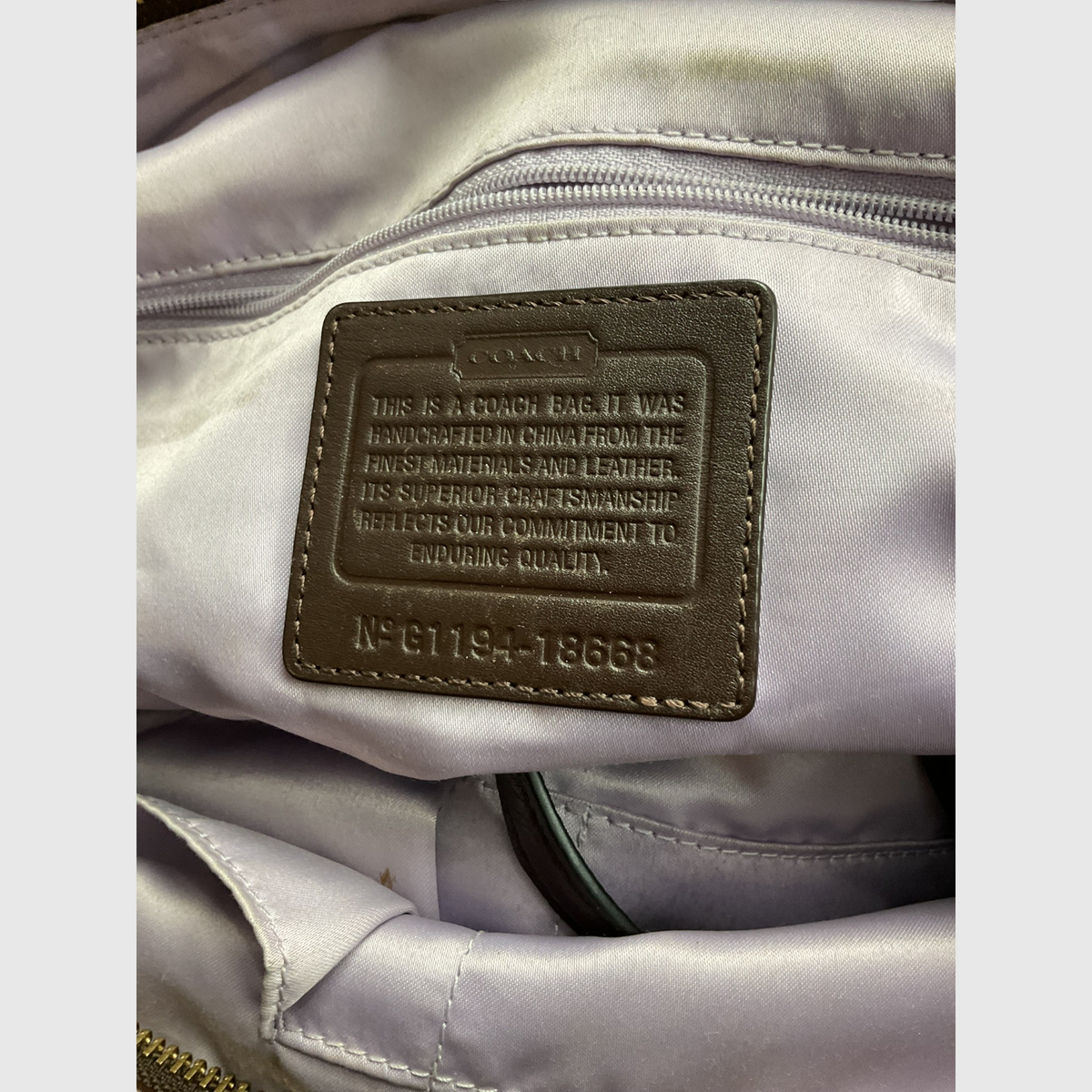 The interior of a gray canvas tote bag with dark brown leather trim and shoulder strap, worn crossbody against a light gray studio background.