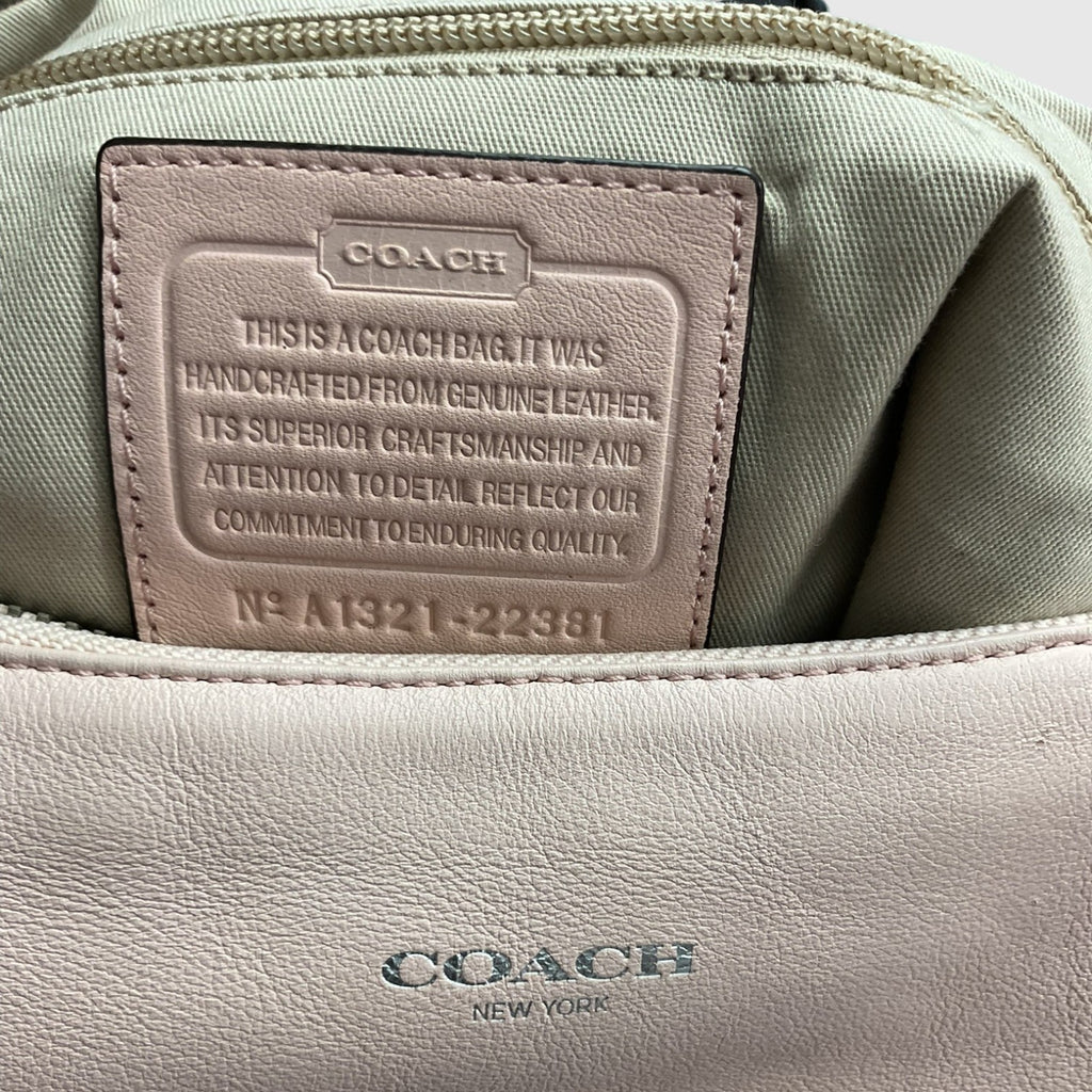 Close-up of the interior of a Coach bag showing a light beige leather patch with embossed text and a sage green fabric lining. The exterior lower portion shows a light beige leather surface with the Coach New York logo embossed.