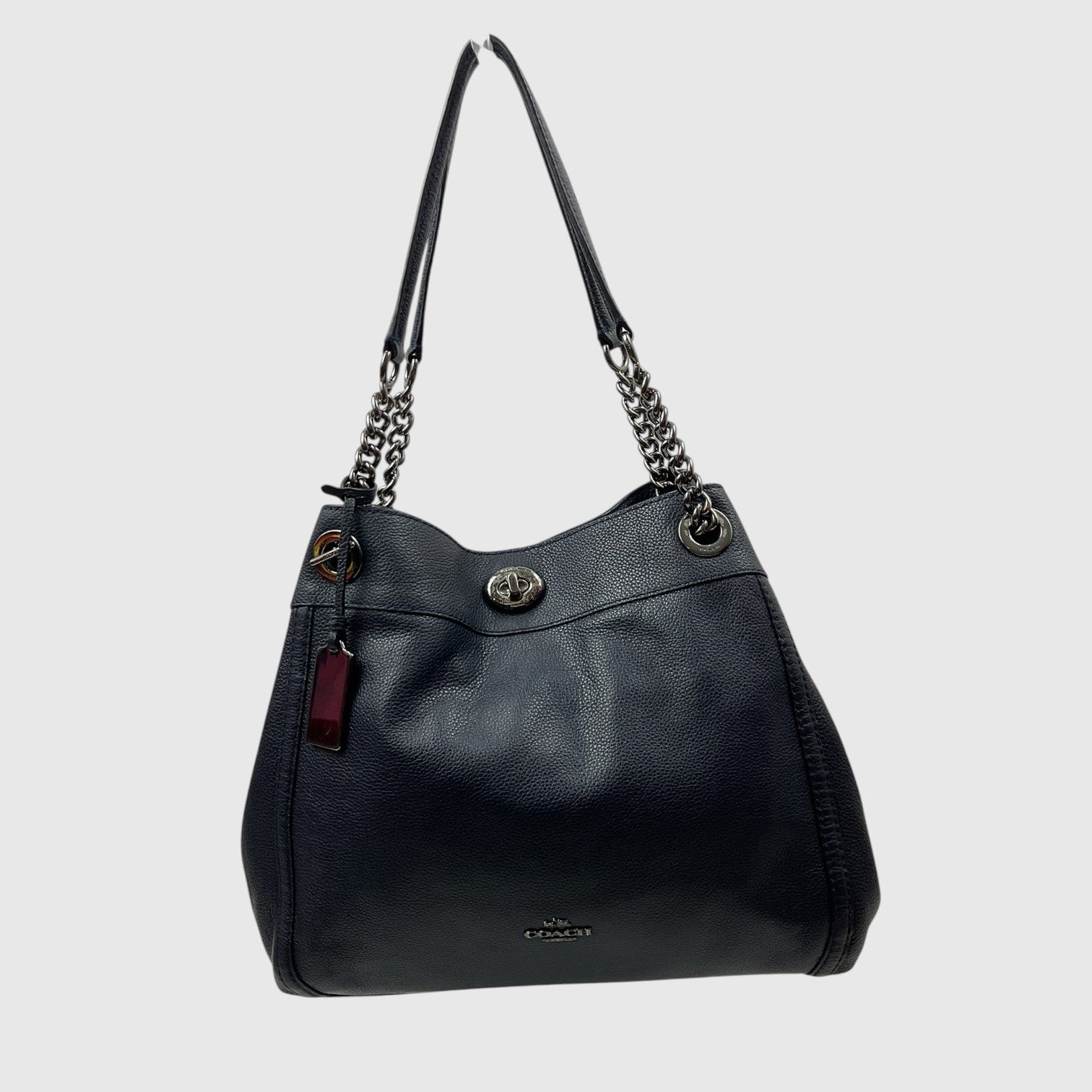 A Coach black pebbled leather hobo shoulder bag with silver-tone chain strap details and a small red leather hangtag, shown against a light gray background.