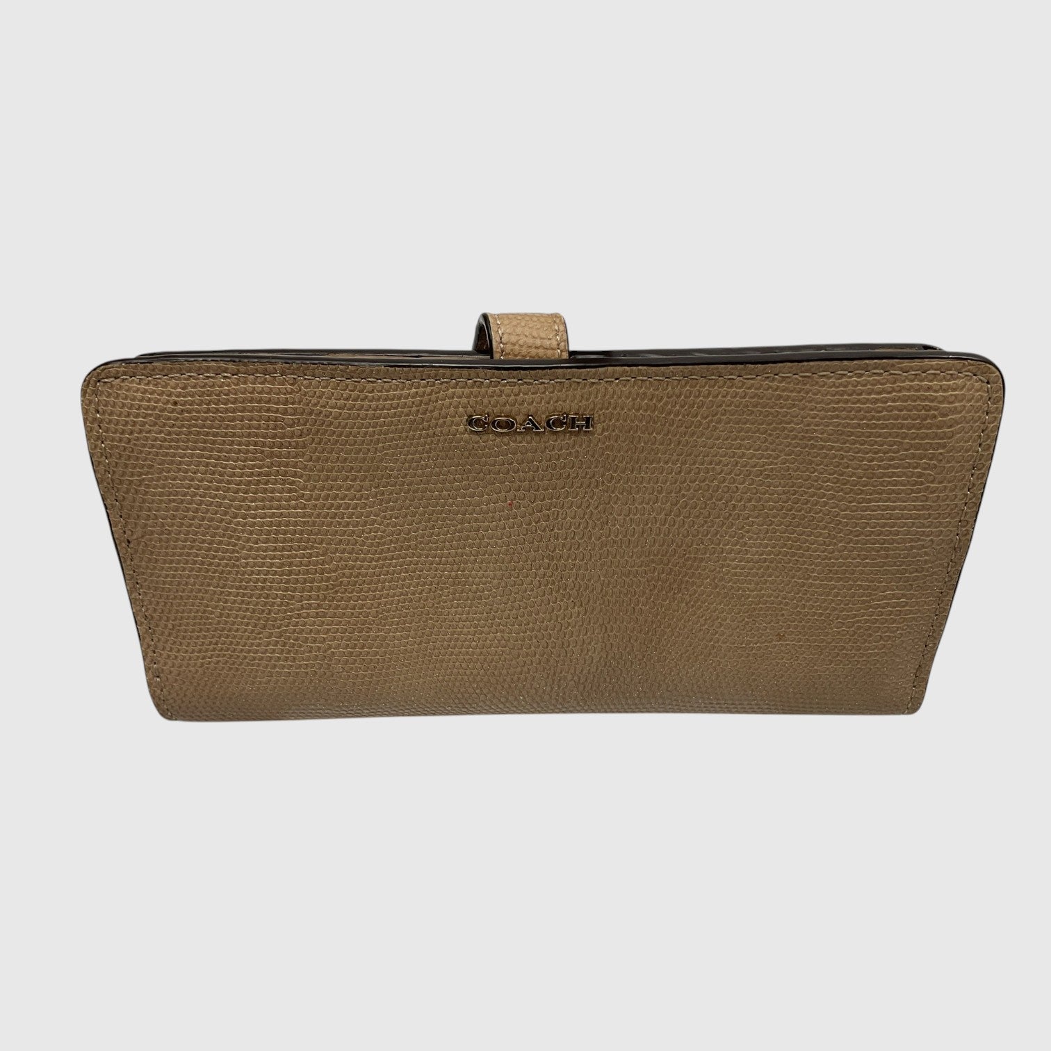 A rectangular clutch bag with a textured leather exterior in a warm brownish-tan color, featuring a small top handle and a debossed logo on the front, set against a solid light gray background.