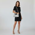 A woman modeling a black short-sleeve mini dress and silver textured shoulder bag against a light gray studio background.