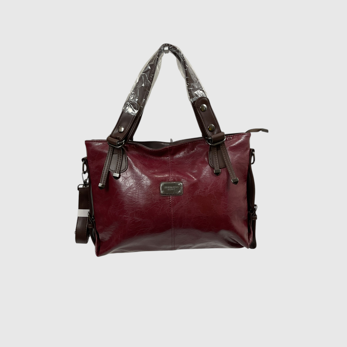 A burgundy faux-leather handbag with dark brown leather straps and trim, featuring a protective plastic wrap on the handles, set against a plain light gray background.