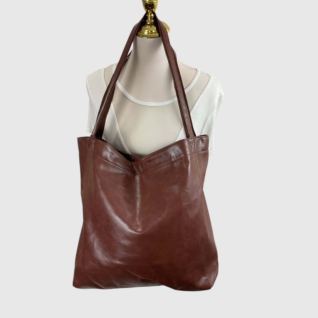 A brown leather tote bag with long shoulder straps, displayed on a cream-colored mannequin torso against a light gray background.