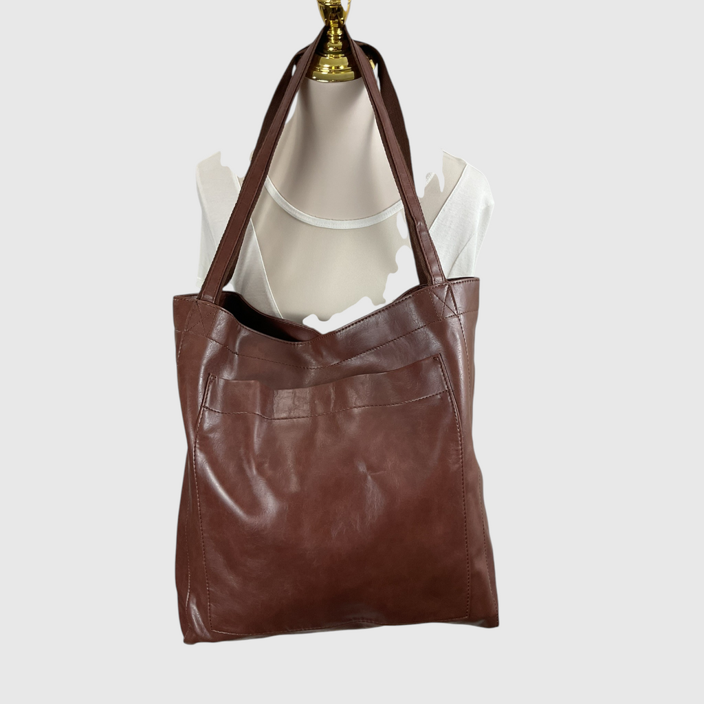 A brown leather tote bag with dual shoulder straps, displayed on a cream-colored mannequin torso with a gold neck cap against a light gray background.