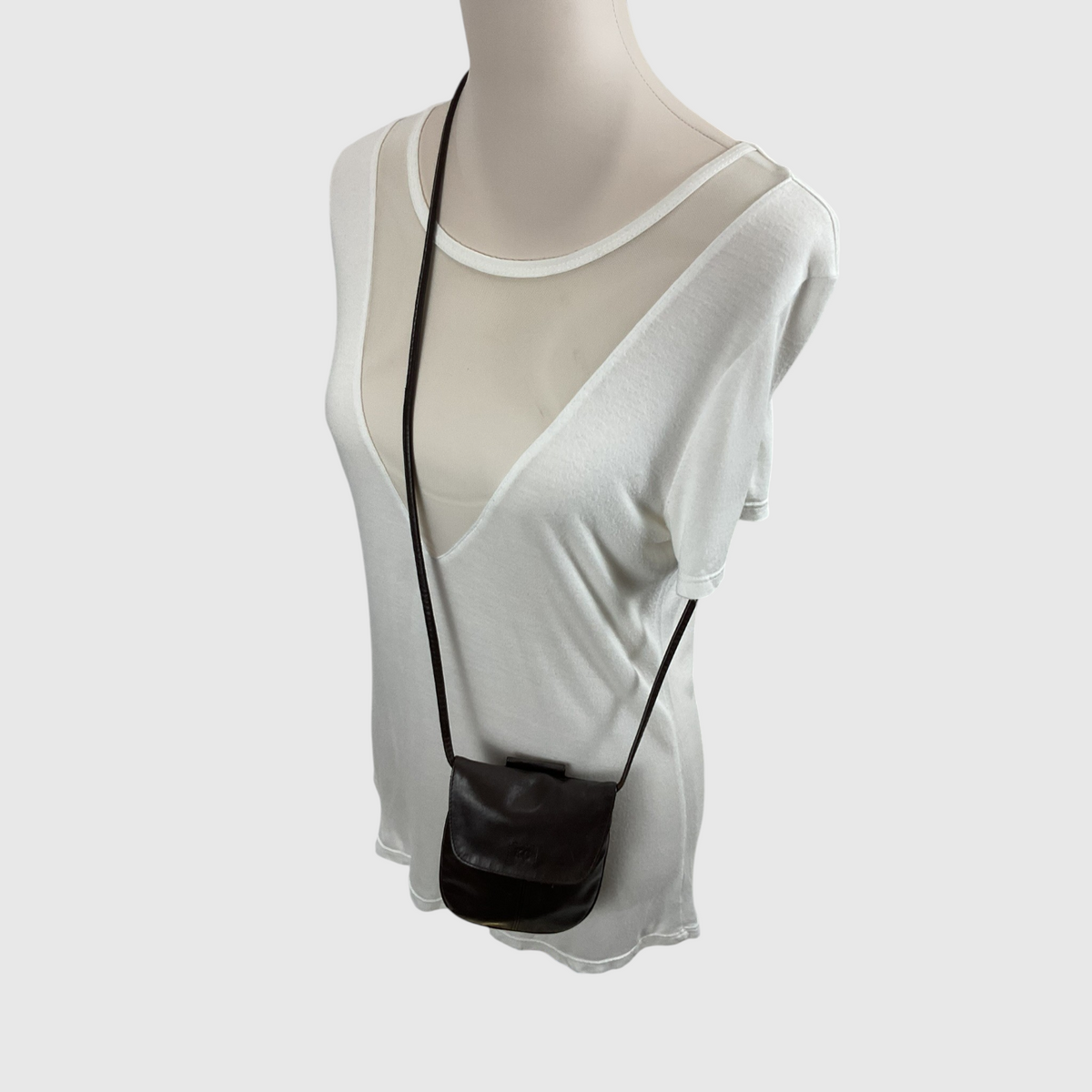 The Solid Smooth Faux Leather  Mini Crossbody Bag on a mannequin wearing a white top against a gray background. 