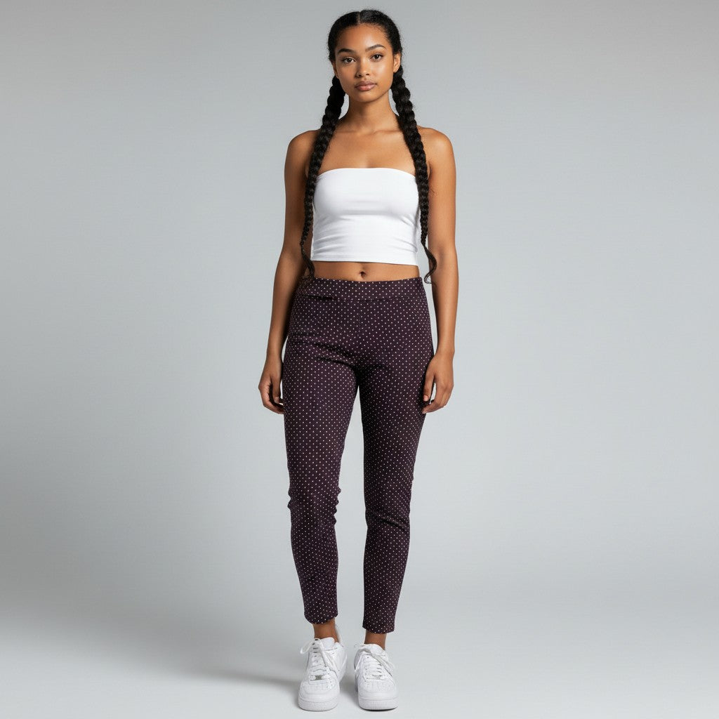 A woman modeling a pair of dark purple cropped pants with a small white polka dot pattern, paired with a white strapless crop top and white sneakers, against a light gray studio background.