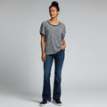 A woman modeling a black and white horizontally striped short-sleeve t-shirt with dark blue flare jeans and black sneakers, standing against a light gray studio background.