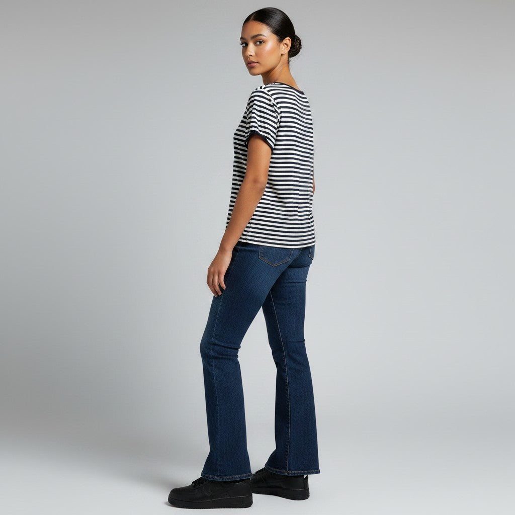 A woman modeling a black and white horizontally striped short-sleeve t-shirt and dark blue flared jeans, shown from a side-back angle against a light gray studio background.