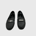 A pair of black Coach loafers with silver-tone metal logo plates on the vamp, displayed against a light gray background.