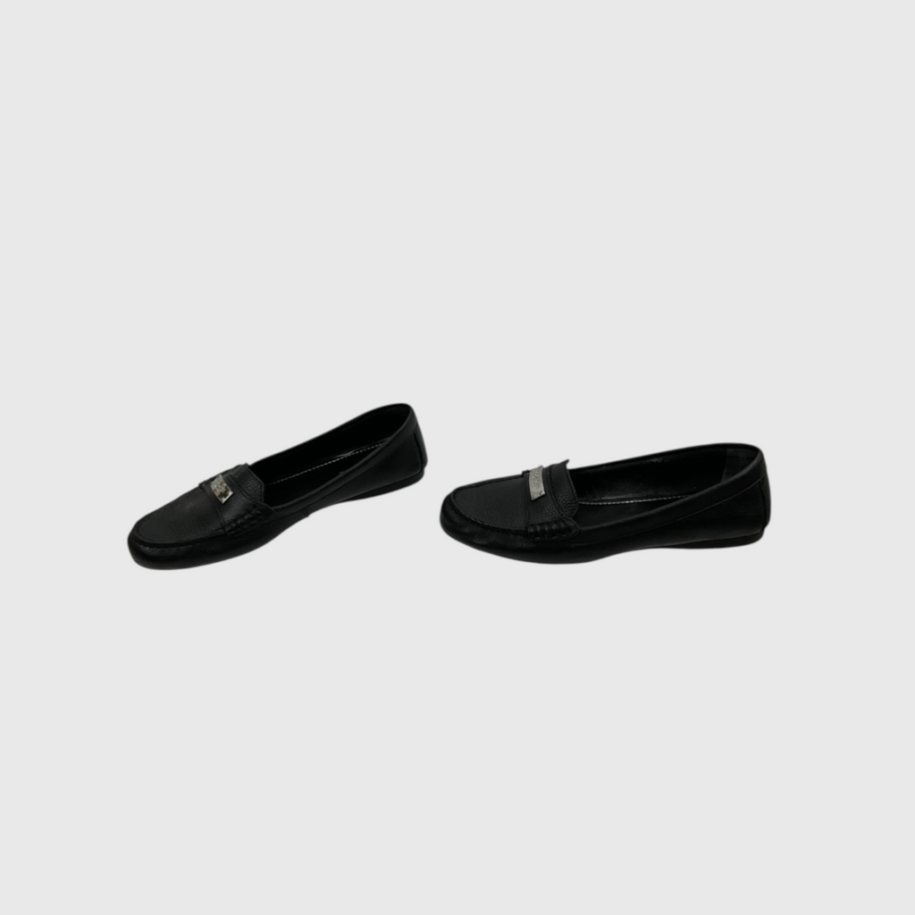 A pair of black leather slip-on loafers with a small silver-tone metal accent on the vamp, displayed against a light gray background.