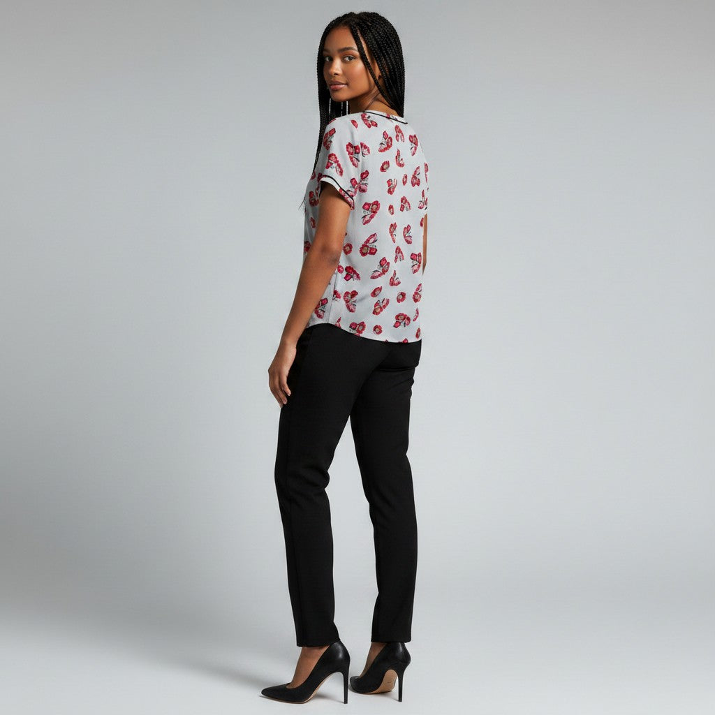 A woman modeling a white short-sleeve top with a red and black paisley pattern, paired with black pants and black high heels, photographed against a light gray studio background.