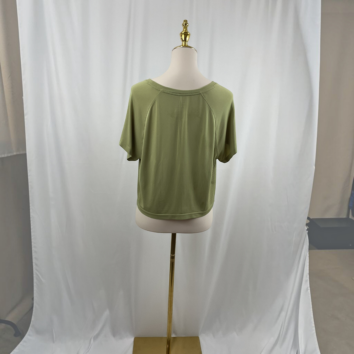A woman wearing a green shirt, white jeans, and black high heels on a studio gray background.
