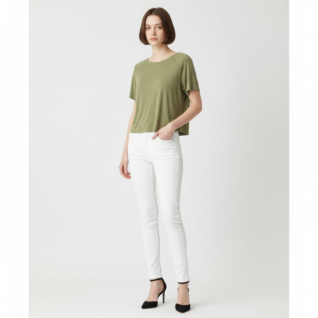 A woman wearing a green shirt, white jeans, and black high heels on a studio gray background.